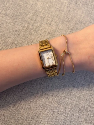 Guldfärgad fyrkantig klocka från Regal - Säljer en elegant guldfärgad klocka från Regal med rektangulärt ur och vit urtavla. Klockan har en klassisk länkarmband i metall och stilrena detaljer. Perfekt för dig som vill ha en snygg accessoar som sticker ut. Den är helt ny och aldrig andvänd. Ord pris 500kr