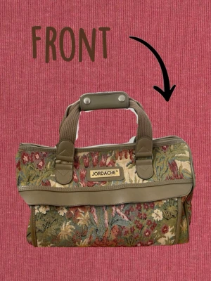 Retro handväska från Jordache - Unik handväska från Jordache med blommigt gobelängtyg i gröna, röda och beige toner. Väskan har bruna handtag och detaljer i konstläder samt dragkedja upptill. Perfekt för dig som gillar retro-stil och vill sticka ut med en färgglad accessoar. På undersidan framkommer svarta fläckar som borde gå att få bort relativt enkelt. Men dessa syns inte vid användning. Därav är priset diskuterbart