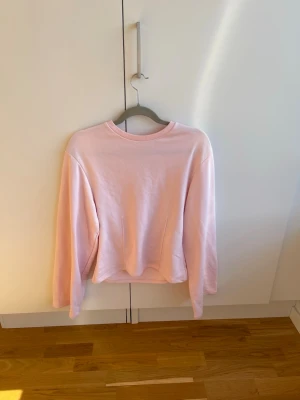 Ljusrosa sweatshirt utan huva - En enkel och stilren ljusrosa sweatshirt med rund hals och långa ärmar. Tröjan har en relaxed fit och är tillverkad i mjukt bomullsmaterial. Perfekt för en chill och avslappnad look.