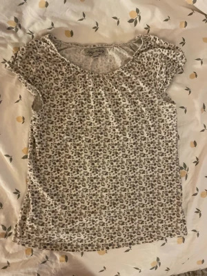 Leopardmönstrad topp från Amy & Iucy barn st 122/128 - Kortärmad topp från Amy & Iucy med leopardmönster i beige och bruna toner. Rund halsringning och mjukt, tunt material som känns skönt mot huden. Vid storlekslappen är där fyra små hål men inget som syns när du har på tröjan. Barn storlek 122/128