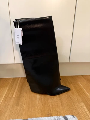 Svarta höga stövlar  - Säljer ett par mörk bruna höga stövlar i glansigt skinnimitation. Stövlarna har spetsig tå och bred, rak skaft som går upp till knät. Perfekta för att lyfta vilken outfit som helst med sin stilrena och trendiga look.