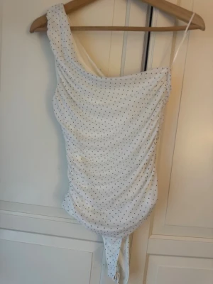 Vit body med svarta prickar - stradivarius  - Superfin vit body med svarta prickar och trendig asymmetrisk "one shoulder"-design. Plagget har snygg drapering (rynkade detaljer) längs sidorna vilket ger en mycket smickrande passform. Helt ny, har xs-m som referens.