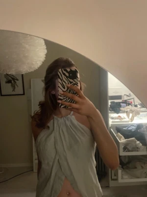 Ljusgrå ärmlös linnetopp - Snygg ljusgrå linnetopp med halterneck och omlott-detalj framtill. Toppen är ärmlös och har en luftig passform, perfekt för varma dagar. Enkel och stilren design som passar till många olika outfits. (Den är inte struken på bilden )