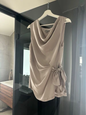 Beige omlott topp med knyt - Säljer en stilren beige topp med omlott-design och knyt i sidan.