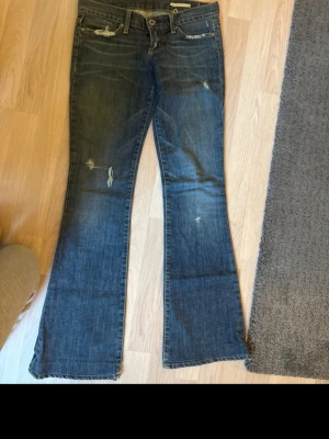 Blå bootcut jeans - Säljer ett par blå bootcut jeans med slitna detaljer. Gammla vintage  jeans från 1900 talet i storlek 25. 