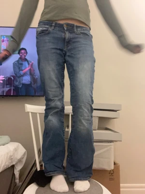 Blå bootcut jeans  - Ett par blå bootcut jeans med låg midja och ett litet hål som syns på bilden. Köpt från vero Moda och storlek XS/S 