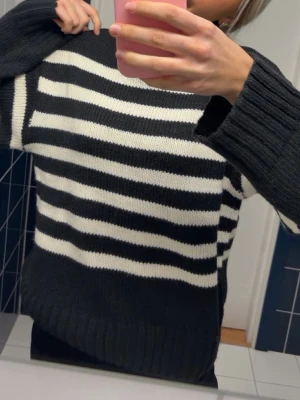 Svartvit randig polotröja stickad NA-KD - Stickad tröja med breda svarta och vita ränder och hög polokrage. Tröjan har långa ärmar och ribbstickade muddar vid ärmslut och nederkant. Perfekt för kalla dagar och ger en klassisk, avslappnad look.
