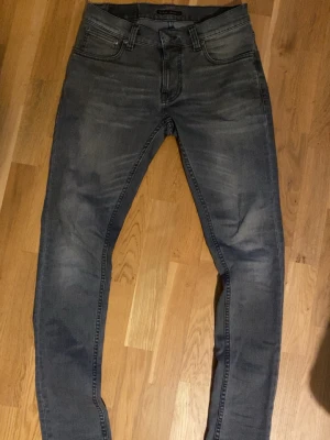Grå Tight Terry Nudie jeans - Säljer ett par grå slim fit jeans från Nudie Jeans med klassiska fem fickor och svarta sömmar på bakfickorna. Jeansen har en snygg tvättad look och är tillverkade i mjukt denimtyg med stretch för extra komfort. De är i modellen tight terry och sitter ganska tight i vaderna ( på mig iaf) Hör av er vid minsta fundering! Storlek: W29 L32