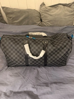 Rutig svart weekendbag liknar Louis Vuitton - Säljer en stor och rymlig weekendbag 55L som liknar Louis Vuitton i klassiskt rutigt mönster. Väskan är svart och grå med detaljer i skinn och har dubbla handtag samt silverfärgad dragkedja. Perfekt för weekendresor och har en riktigt clean look. 