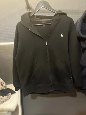 Svart hoodie från Polo Ralph Lauren - Ralph Lauren zip up i svart färg, storlek M. Snöret som går igenom tröja  har jag tagit bort men kan sätta tillbaka till önskan.  Kontakta om du har frågor osv
