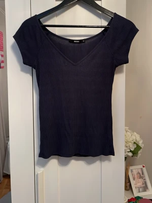 Marinblå ribbad topp från Bik Bok - Säljer en marinblå ribbad topp från Bik Bok med v-ringad hals och korta ärmar. Toppen har en slim passform, enkel men fin vardags topp.Materialet är mjukt och stretchigt.