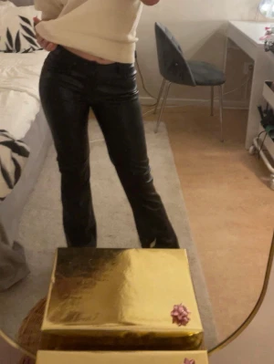 Svarta coated jeans med rak passform - Säljer ett par svarta läderbyxor med utsvängning och låg midja. Snygg glansig finish som ger en cool look, perfekta till en trendig outfit. Klassisk femficksmodell och dragkedja fram.