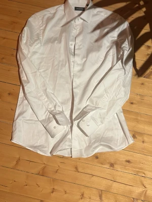 Vit klassisk skjorta från Dressmann - Säljer en stilren vit skjorta från dressman med klassisk krage och knappar framtill. Skjortan är långärmad perfekt för en clean och snygg look. Passar till många olika outfits och tillfällen.