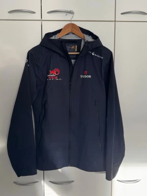 Limited edition sailracing jacka - ✨Nypriss:4000kr✨                                                 Mörkblåe Limited edition vindjacka från Red Bull Racing med dragkedja framtill, huva och loggor från Red Bull, Tudor och Sail Racing. Jackan har två sidofickor med dragkedja och sportig design. Materialet är lätt och vattenavvisande, perfekt för blåsiga dagar. Storlek S men passar även M