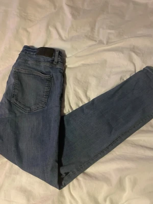 Blå slim fit jeans från Dressmann - Snygga blå jeans från Dressmann i modellen slim fit. Klassisk femficksdesign med normalhög midja och dragkedjegylf. Jeansen är tillverkade i bomull med en liten stretch för extra komfort. Perfekta för en avslappnad och stilren look.