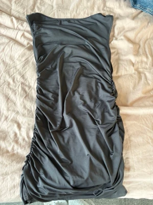 Grå kort klänning med rynkade sidor - Säljer en figursyd klänning. Öppen i ryggen. Använd en gång. Storlek M💕