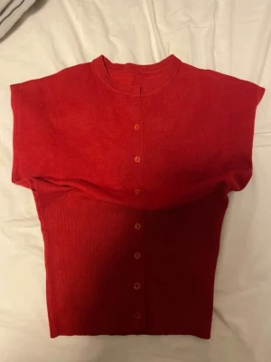 Röd kortärmad kofta med knappar - Snygg röd kortärmad kofta med rund hals och knappar framtill. Materialet är stickat och mjukt. Använd aldrig, passar inte riktigt i röd färg därför säljer jag. 
