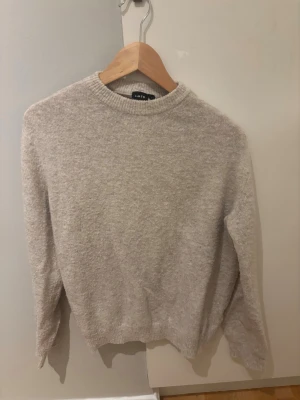 Beige stickad tröja från LMTD - En enkel och stilren beige stickad tröja från LMTD med rund halsringning och ribbade muddar. Perfekt för lager-på-lager och passar till många olika outfits. Materialet är mjukt och ger en avslappnad look. Modellen är 175 cm lång och storleken är 13-14 år.