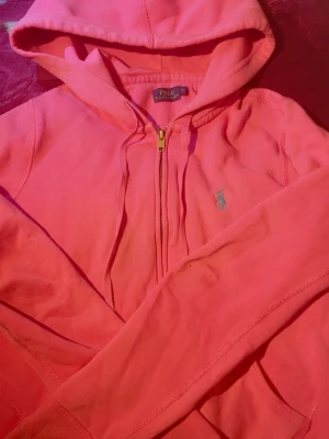 Rosa/coral hoodie från Polo Ralph Lauren - Snygg rosa hoodie från Polo Ralph Lauren med dragkedja framtill och klassisk huva. Broderad logga på bröstet och mjukt bomullsmaterial. Perfekt för en avslappnad och sportig stil. Använd endast 2 gånger❤️Storlek S men passar som Xs lika bra. Priset kan självklart diskuteras också❤️