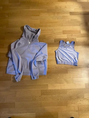 Ljuslila hoodie och tank top set från Kappahl - Ljuslila hoodie från Kappahl med halv dragkedja framtill och huva. Hoodien har ribbade muddar vid ärmslut och nederkant. Perfekt för en avslappnad och sportig stil. I samband med en ljuslila sports top.