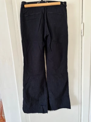 Randiga kostymbyxor från Acne Studios - Snygga svarta kostymbyxor från Acne Studios med diskreta vita kritstrecksränder. Byxorna har raka ben och två bakfickor. Perfekta för en stilren och trendig look.