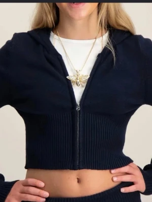 Mörkblå cropped hoodie med dragkedja - Trendig mörkblå cropped stickad tröja med dragkedja framtill och ribbstickad nederdel. Tröjan har långa ärmar och en snygg, figurnära passform. Perfekt för dig som gillar en modern och avslappnad look. Materialet är mjukt och stretchigt stickat tyg.