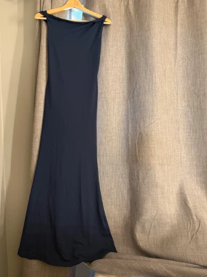 Marinblå långklänning  - Elegant marinblå långklänning. Den är aldrig använd, helt ny. meningen är att man ska ha banden på sidan av axlarna och den har figurnära passform. Klänningen har en minimalistisk design utan synliga detaljer eller mönster, vilket ger ett stilrent och tidlöst intryck. Perfekt för dig som ska ha bal eller skolavslutning. 