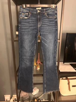Blå bootcut jeans med rå kant - Säljer ett par blå bootcut jeans med rå kant nertill. Jeansen har klassisk femficksmodell, normal midja och kontrastsömmar. Materialet är denim i bomull med lite stretch för extra komfort. Perfekta för en avslappnad och trendig look.