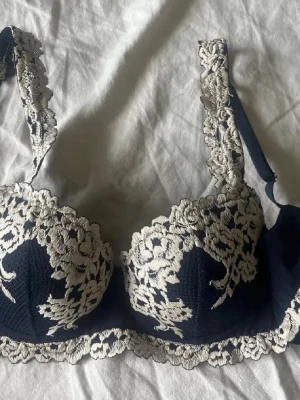 Mörkblå spets-bh från Intimissimi - Snygg mörkblå bh från Intimissimi med vacker vit spetsdetalj över kupor, band och nederkant. Bh:n har vadderade kupor och breda axelband med spets. Perfekt för dig som gillar en feminin och elegant stil.