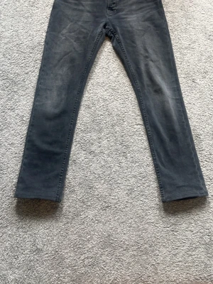 Mörkgrå jeans från Nudie Jeans - Snygga mörkgrå jeans från Nudie Jeans med raka ben och klassisk femficksdesign. Jeansen har diskreta slitningar och broderade bakfickor. Perfekta för en avslappnad och trendig stil. Jeansen är upplagda från L32 till vad som skulle motsvara L31. Nypris: 1600kr mitt pris: 800kr