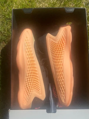 AE 1s orange/svart basketskor - EU 45 1/3 - Snygga Adidas Yeezy 700 V3 sneakers med orange sula och svarta meshpaneler upptill. Skorna har en futuristisk design med honeycomb-mönstrad sula och svarta snören. Perfekta för dig som gillar streetwear och vill sticka ut.Ett par basketbollskor AE1, Anthony Edwards 1, i orange och svart. Skorna har en distinkt design med en mönstrad sula och kommer med extra skosnören i rött. Helt oanvända med lapp kvar.  Nypris: 1349kr