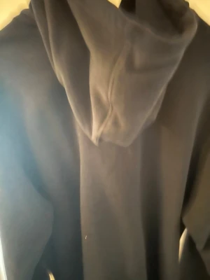 Svart hoodie från Nike - Klassisk svart hoodie från Nike med huva och magficka. Diskret Nike-logga på bröstet. Tillverkad i mjukt material som känns skönt mot huden. Perfekt för en avslappnad och sportig stil.