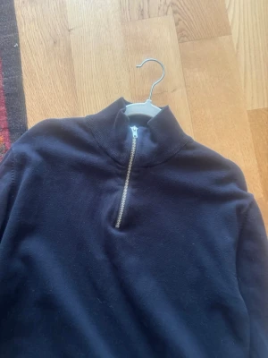 Svart halvzip tröja med hög krage Jack and Jones - En svart tröja med halv dragkedja och hög krage. Tröjan har långa ärmar och ribbade muddar vid ärmslut och nederkant. Perfekt för lager-på-lager och chill stil.
