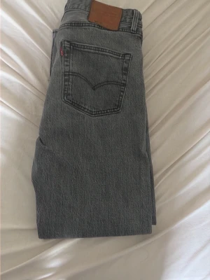 Grå Levi's 501 jeans straight fit - Säljer ett par klassiska grå Levi's 501 jeans med rak passform och femficksdesign. Jeansen har en snygg vintage-look, ikonisk bakficka med söm och läderpatch i midjan. Perfekta för en avslappnad och tidlös stil.