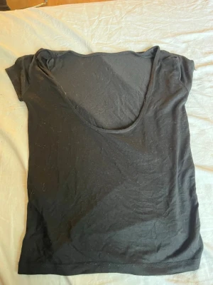 Svart t-shirt med liten öppen rygg - En svart t-shirt med korta ärmar och lite öppen i ryggen. Enkel och stilren design som passar till det mesta. Tillverkad i mjukt material som känns skönt mot huden.