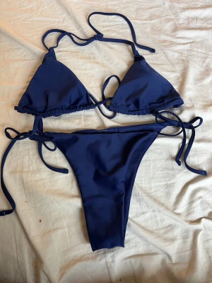 Mörkblå trekantsbikini med knyt - Snygg mörkblå bikini med klassisk trekantsmodell upptill och knyt både vid rygg och höfter. Bikinin är tillverkad i ett stretchigt material som känns bekvämt mot huden. Perfekt för stranden eller poolen.Med två olika bikini underdelar till
