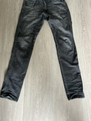 Svarta slim fit jeans från replay - Snygga svarta slim fit jeans från Nudie med klassisk femficksdesign och diskreta slitningar. Jeansen har raka ben och är tillverkade i mjuk denim med stretch för extra komfort. Perfekta för en avslappnad och trendig look. Storlek 32/24