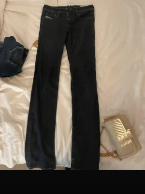 Mörkblå lowwaist bootcut jeans från Diesel - Snygga mörkblå bootcut jeans från Diesel med klassisk femficksdesign och låg midja. Jeansen har subtila slitningar och är tillverkade i stretchigt denim för en bekväm passform. Perfekta för dig som gillar en tidlös och avslappnad stil.