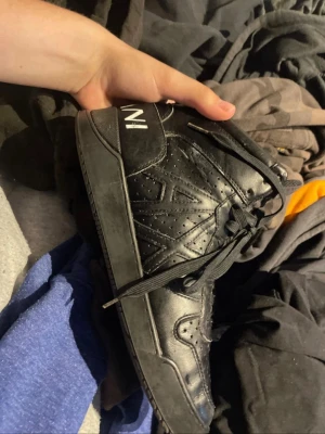 Svarta high-top sneakers från Armani - Säljer ett par svarta high-top sneakers från Armani med snygga detaljer och perforeringar på sidorna. Skorna har snörning, robust sula och logotypen 'ARMANI' tryckt på hälen. Tillverkade i läder med en stilren och modern look.