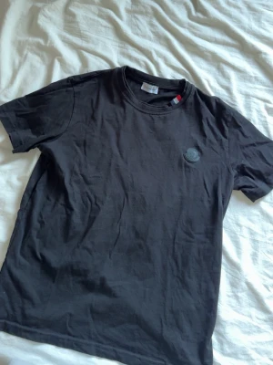 Svart t-shirt i bomull - Snygg svart t-shirt  med rund halsringning och diskret logga på bröstet. Tillverkad i mjuk bomull och har klassisk passform med korta ärmar. Perfekt för en clean och stilren look.