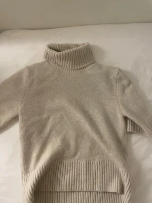 Beige polotröja från H&M - Mysig beige stickad polotröja från H&M med bred ribbstickad polokrage och nederkant. Tröjan har långa ärmar och är tillverkad i ett mjukt material .