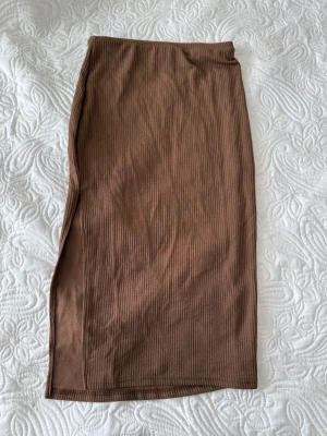 Brun ribbad långkjol från Shein - Säljer en brun ribbad långkjol från Shein i storlek S. Kjolen har en smal passform och en slits på sidan som ger en snygg detalj. Tillverkad i mjukt material som känns skönt mot huden. Perfekt att styla med en enkel topp eller body. Aldrig använt! 