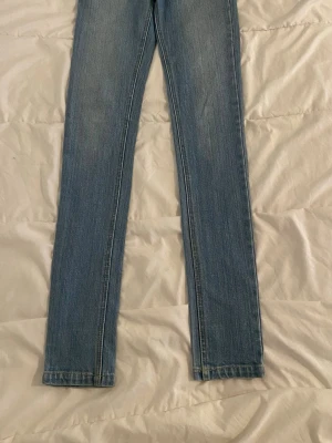 Ljusblå skinny jeans med knappar Från Cheap Monday.  - Säljer ett par ljusblå skinny jeans med hög midja och knappgylf. Jeansen har klassisk femficksdesign och är tillverkade i stretchigt denimtyg för en bekväm passform. Perfekta till en avslappnad look och lätta att matcha med olika stilar.