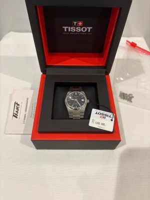 Tissot PRX Powermatic 80 klocka - Snygg Tissot PRX Powermatic 80 35mm herrklocka med silverfärgat armband i rostfritt stål och svart urtavla. Klockan har datumvisning och klassisk rund form. Levereras i originalask med extra länkar och manual. Givetvis äkta. Skicka 9.5/10. 