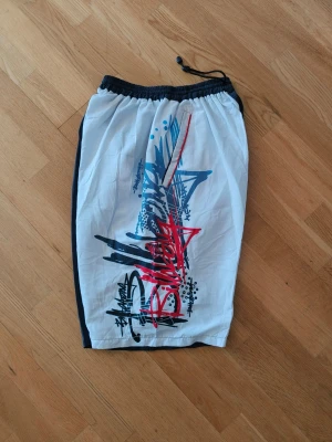 Billabong  - Säljer ett par långa badshorts med elastisk midja och snörning. blått, rött och orange. Perfekta för stranden eller poolen när du vill sticka ut.