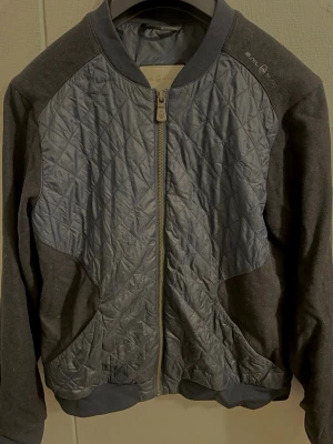 Sweter rozpinany Sail racing, cardigan Sail Racing - Säljer en mörkblå bomberjacka från Sail Racing med quiltad framsida och baksida i polyester. Jackan har ribbade muddar, dragkedja framtill och mjuka ärmar i ullmix. Snygg logga på axeln och nacken. Perfekt för dig som gillar sportig och clean stil.