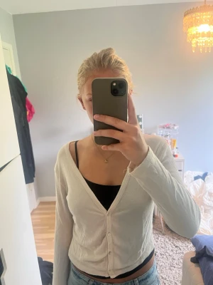 Vit ribbad kofta med knappar - Säljer en vit ribbad kofta med v-ringning och knäppning framtill. Koftan har långa ärmar och är tillverkad i ett tunt, mjukt material som passar perfekt till jeans. Enkel och stilren design.