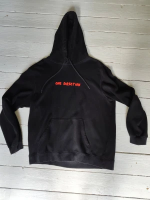 One Direction Hoodie (homemade) - Svart HM hoodie med One Direction tryck. "One Direction" i deras typsnitt på framsidan i rött och den roliga/omskrivna versionen av What Makes You Beautiful på baksidan i blått.