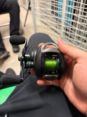 Svart baitcastingrulle med grön lina - Säljer en svart baitcastingrulle med detaljer i grönt och silver. Rullen har två ergonomiska handtag och är laddad med grön fiskelina. Perfekt för dig som gillar sportfiske och vill ha bra kontroll på kastet.