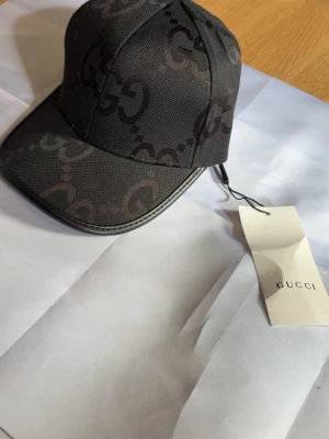 Svart keps från  med GG-mönster - Snygg svart keps från Zara med det klassiska GG-monogrammet i mörkgrått över hela kepsen. Kepsen har böjd skärm och är tillverkad i ett tåligt tygmaterial. Perfekt accessoar för dig som vill ha en exklusiv och trendig look.